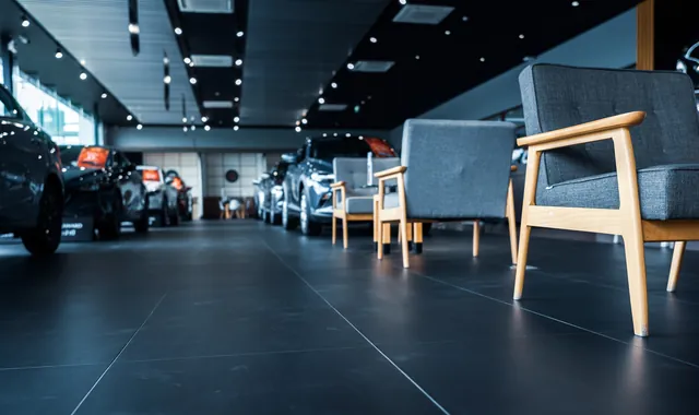 Interior of a modern car dealership showroom with a new vehicle on the display floor, glass frontage and customer seating, no people visible