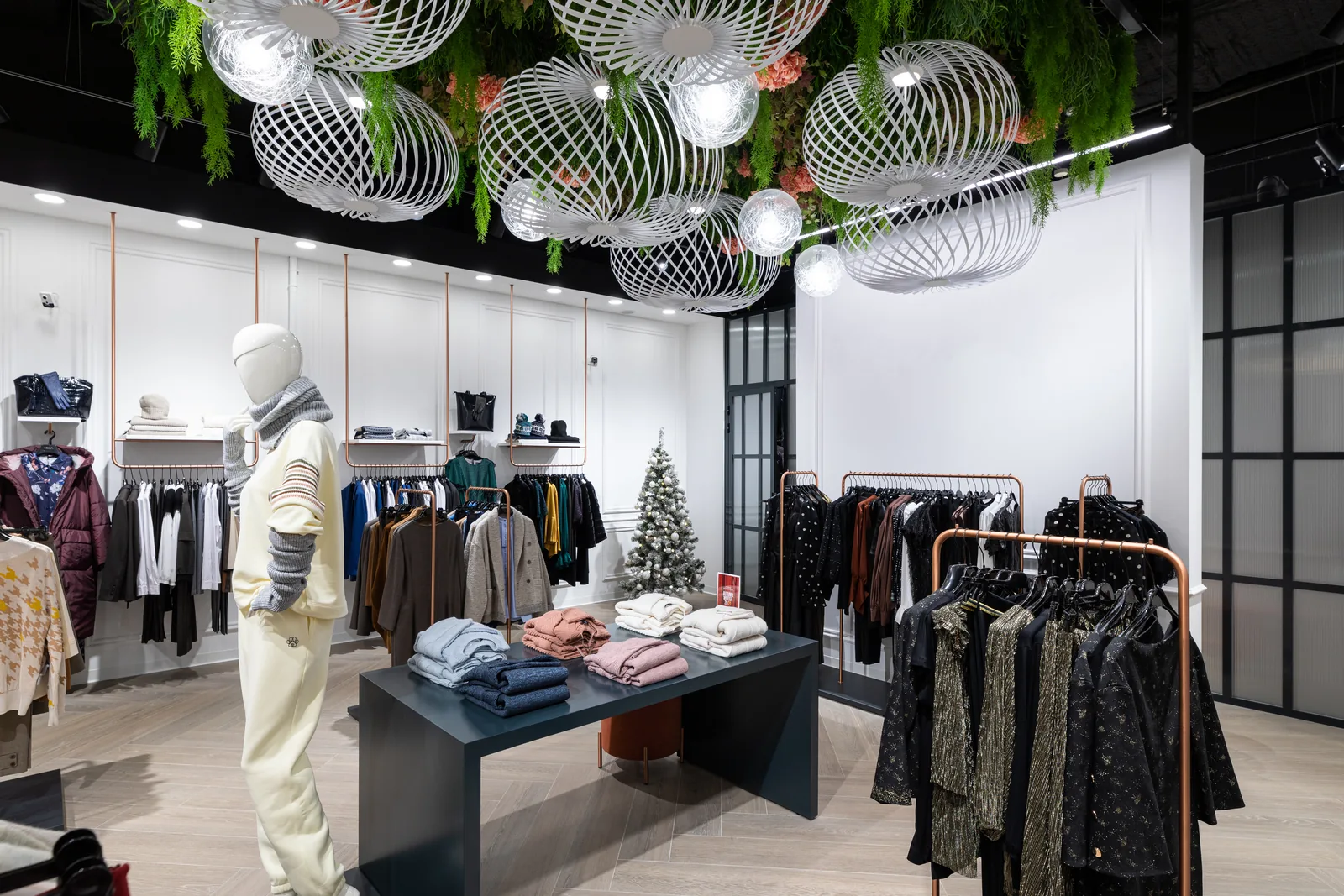 Interior of a modern apparel store with garment rails, folded clothing displays and a fitting-room corridor under overhead ceiling cameras