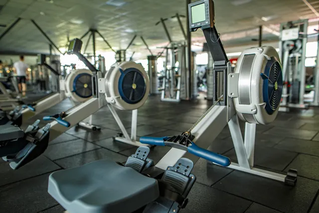Interior of a modern fitness club showing a cardio area, free-weight zone and an overhead camera, with no people identifiable